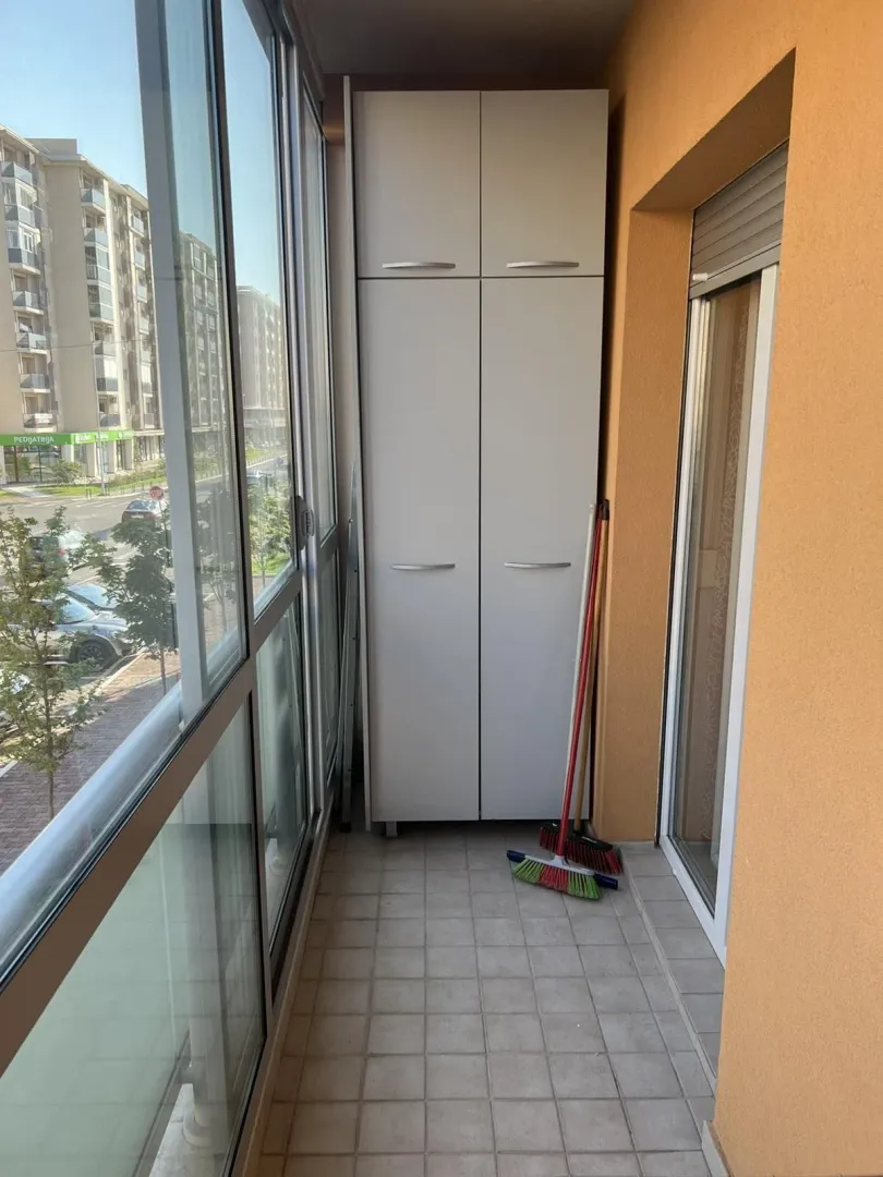 Zastakljeni balkon sa visokim ormarom za odlaganje.