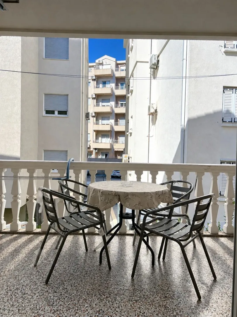 Covered balcony with seating furniture and a view of surrounding buildings.