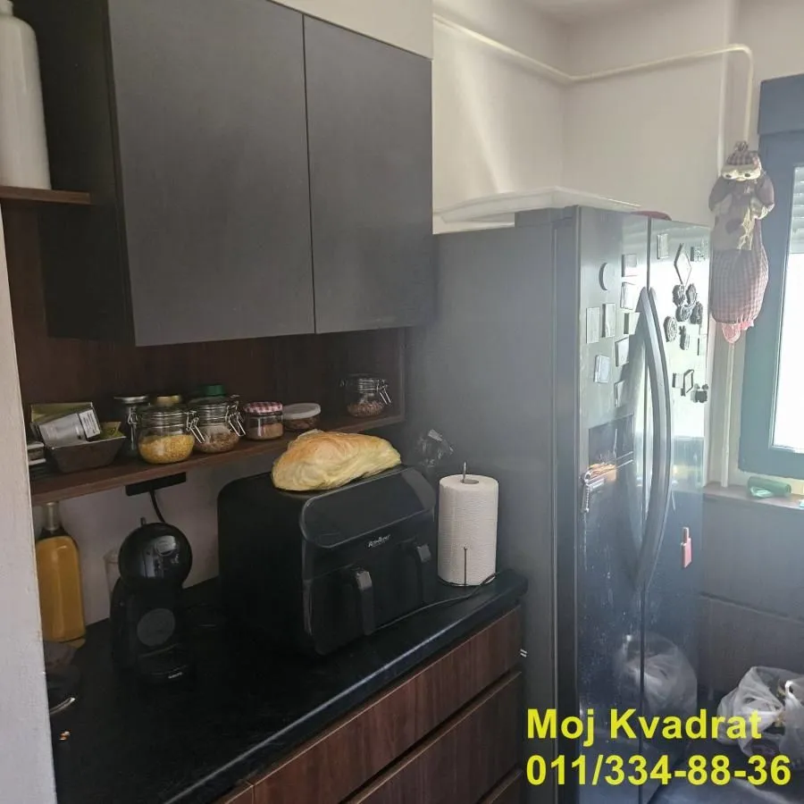 Deo kuhinje sa kuhinjskim elementima, frižiderom i radnom površinom.