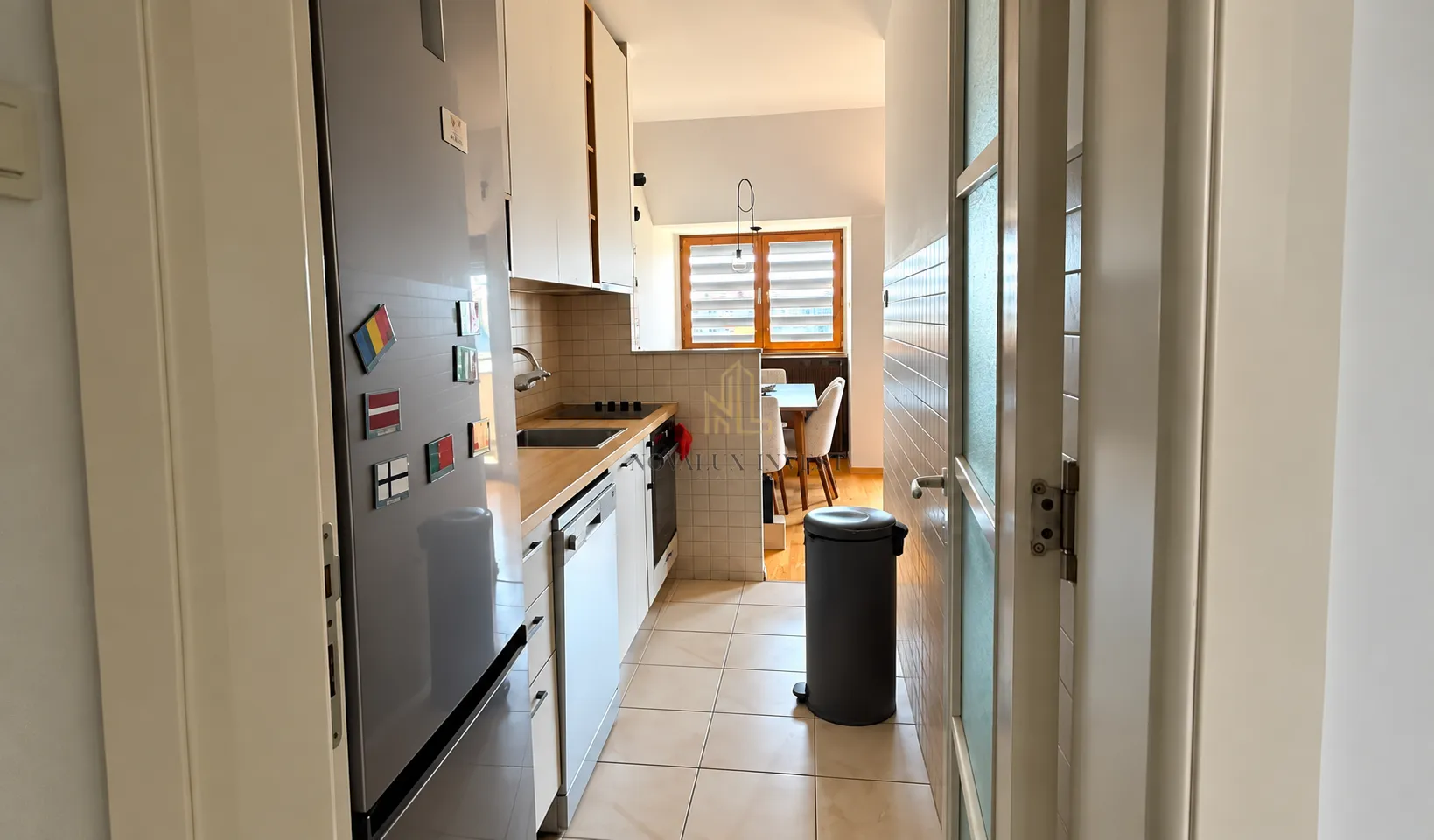 View of a narrow kitchen with a refrigerator and built-in units.