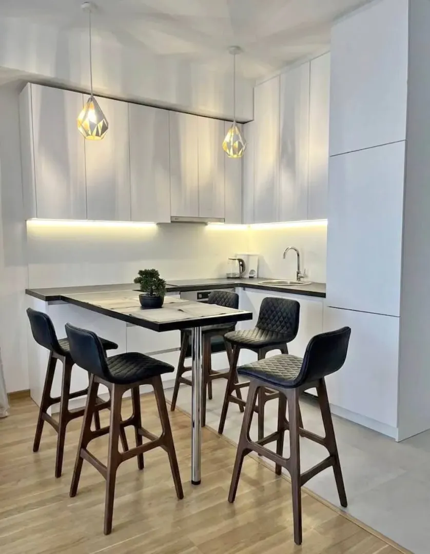 Modern white kitchen with a dining table and bar stools.