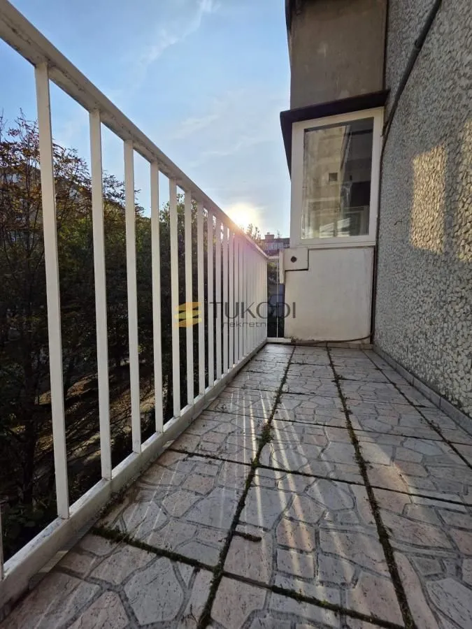 Dugački balkon sa metalnom ogradom i pogledom na zelenilo.