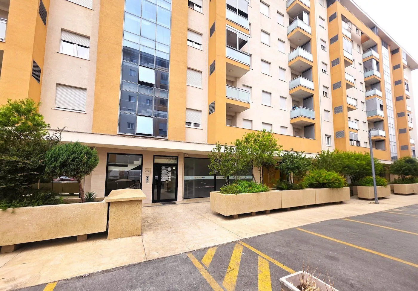 Exterior of a modern residential building with a landscaped entrance and parking.