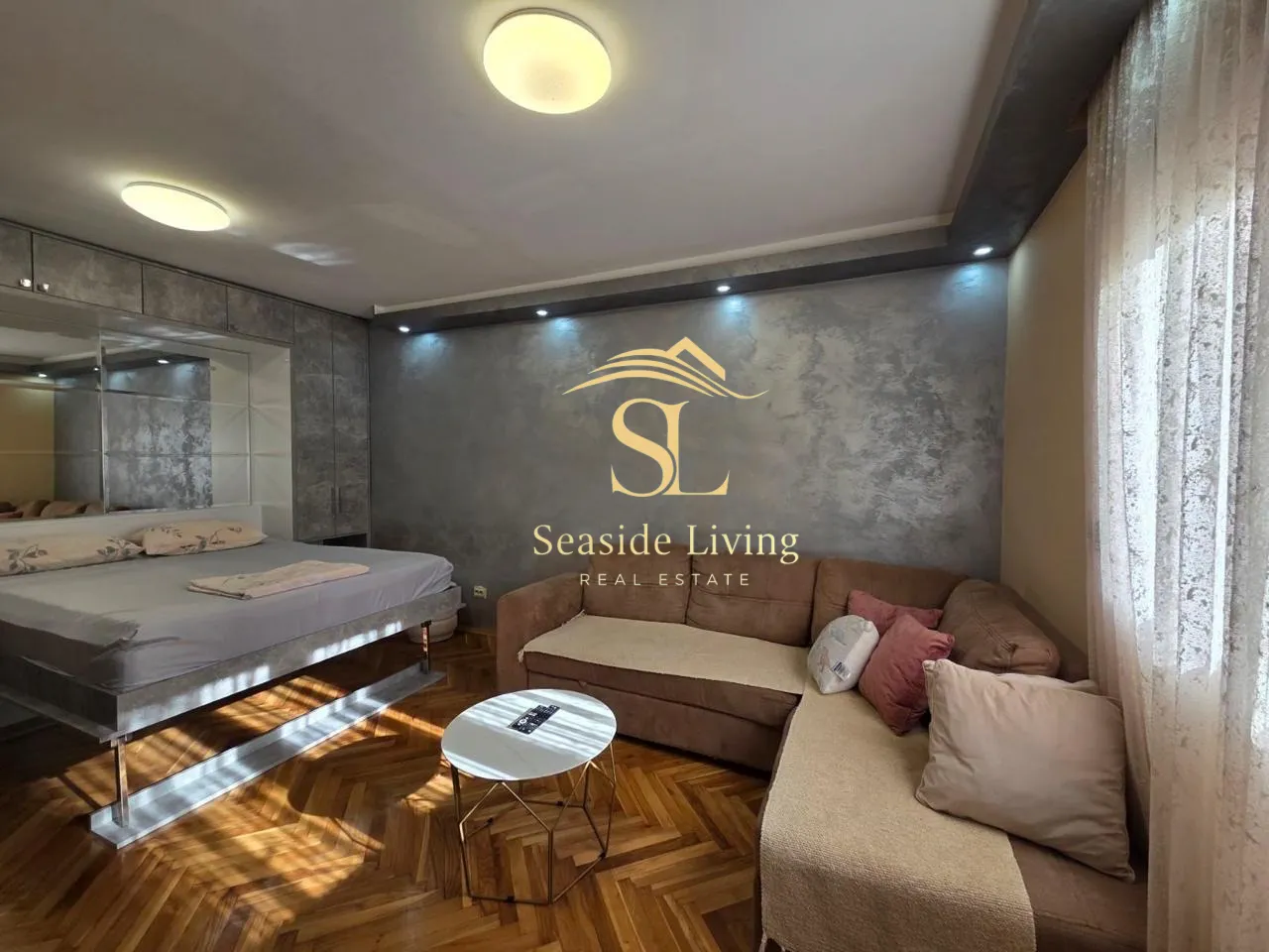 Spacious living room with a corner sofa, bed, and parquet flooring.