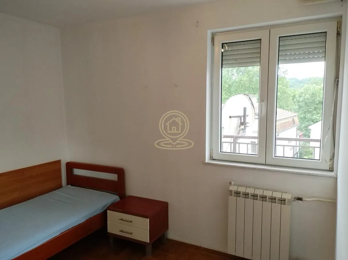 Manja spavaća soba sa krevetom, noćnim stočićem i prozorom.