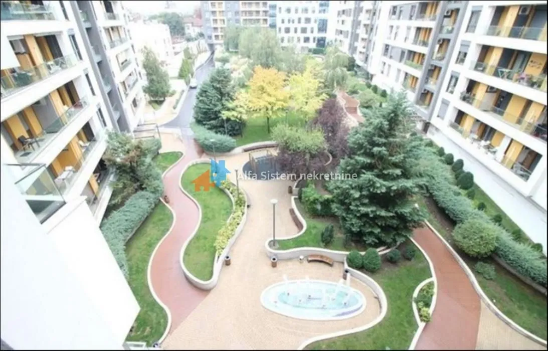 Pogled iz zgrade na uređeno unutrašnje dvorište sa stazama i zelenilom.