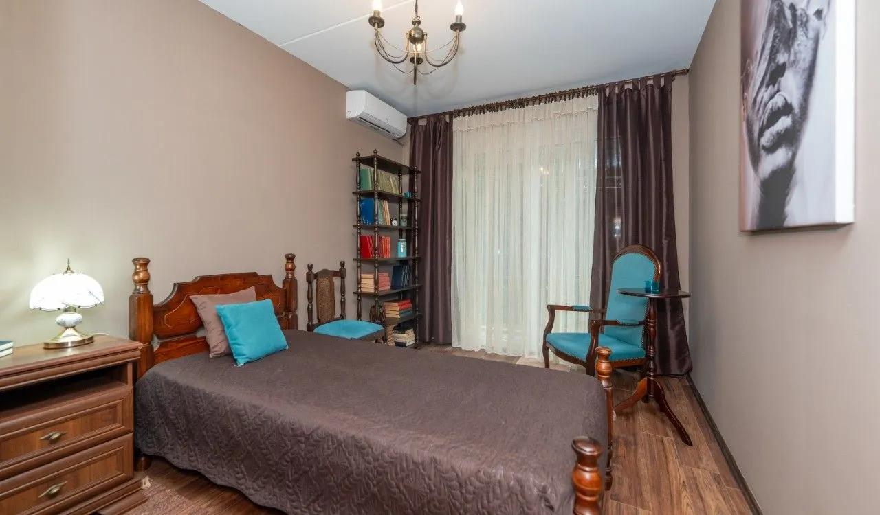 Furnished bedroom with a double bed, blue armchair, and bookshelf.