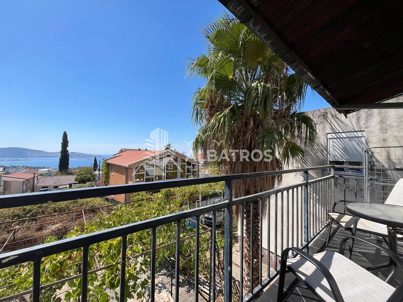 Covered balcony with outdoor seating and a view of the sea and surroundings.