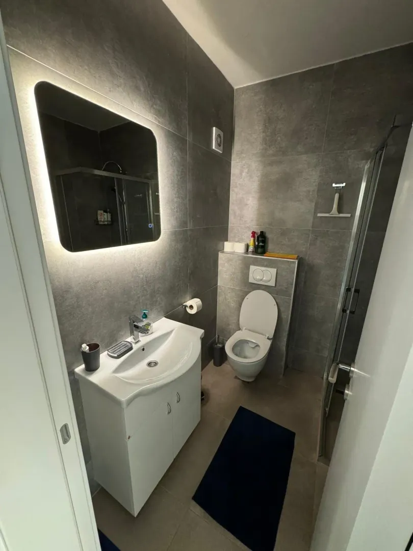 Modern bathroom tiled in grey with a vanity sink, toilet, and shower cabin.