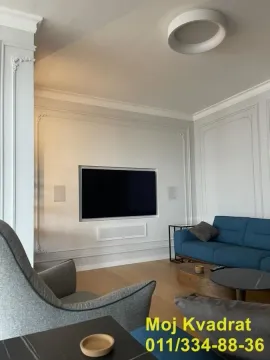 Dnevna soba sa plavom garniturom, foteljom i televizorom na zidu. - image 4