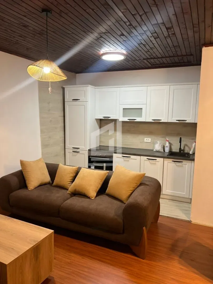 Living room with a sofa and a fitted kitchen in the background.
