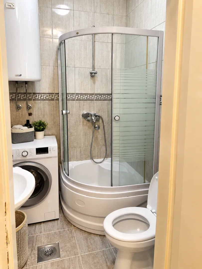 Small bathroom with a shower cabin, sink, washing machine, and toilet.