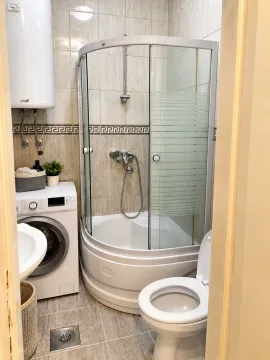 Small bathroom with a shower cabin, sink, washing machine, and toilet. - image 6