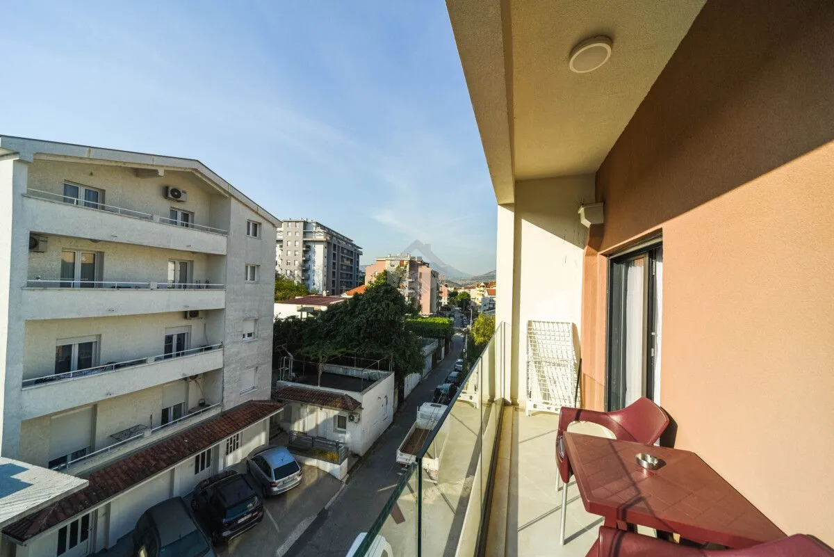 Natkriveni balkon sa garniturom za sjedenje i pogledom na ulicu i okolne zgrade.
