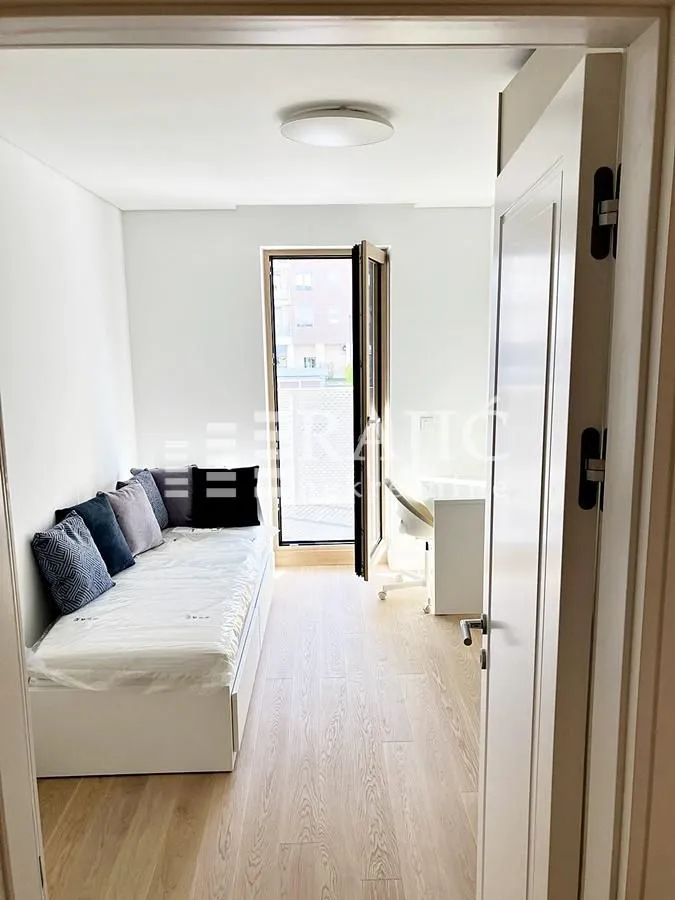 Smaller bedroom with a bed and a desk next to the balcony door.