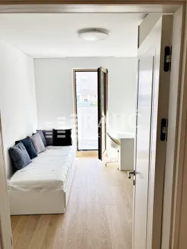 Smaller bedroom with a bed and a desk next to the balcony door. - image 7