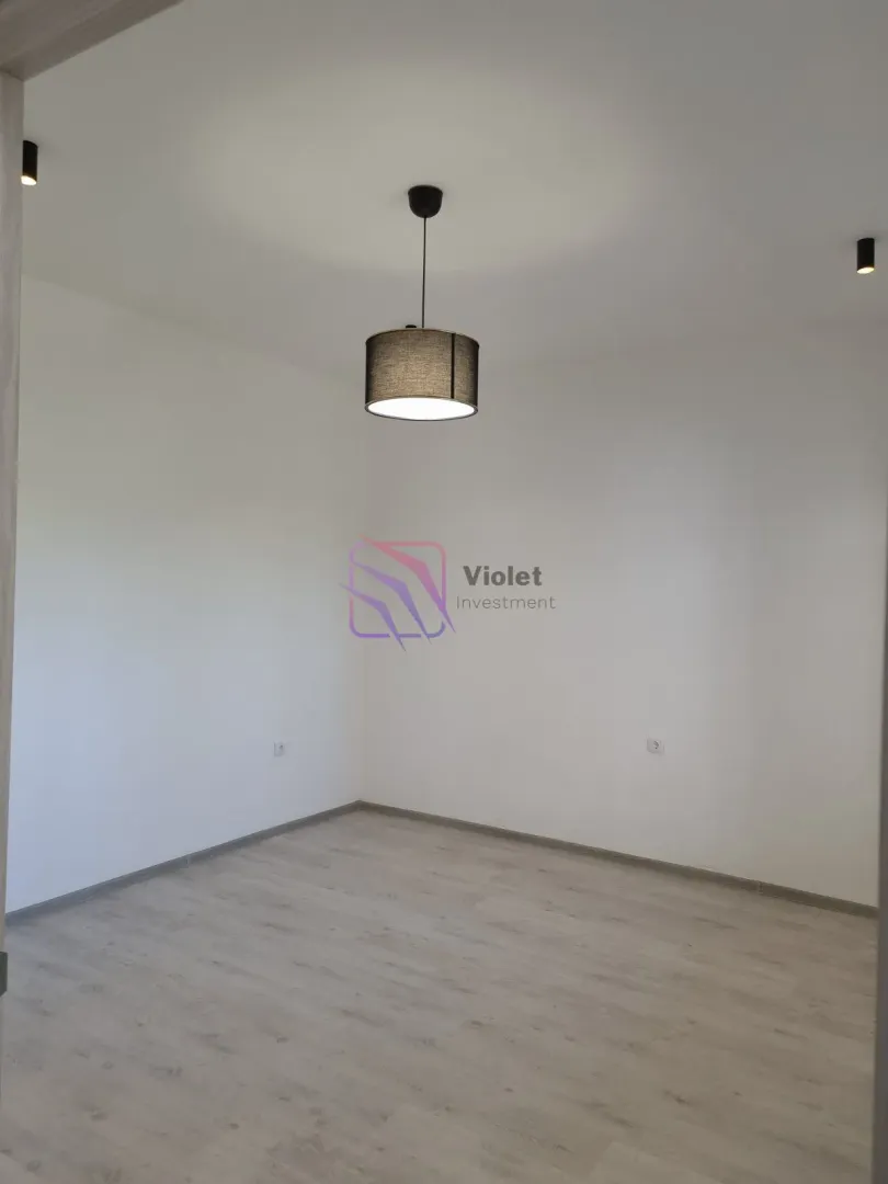 Empty room with white walls, laminate flooring and a pendant light.