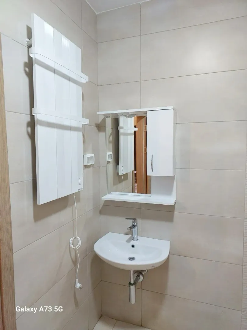 Manje kupatilo sa umivaonikom, ogledalom i bijelim zidnim radijatorom.