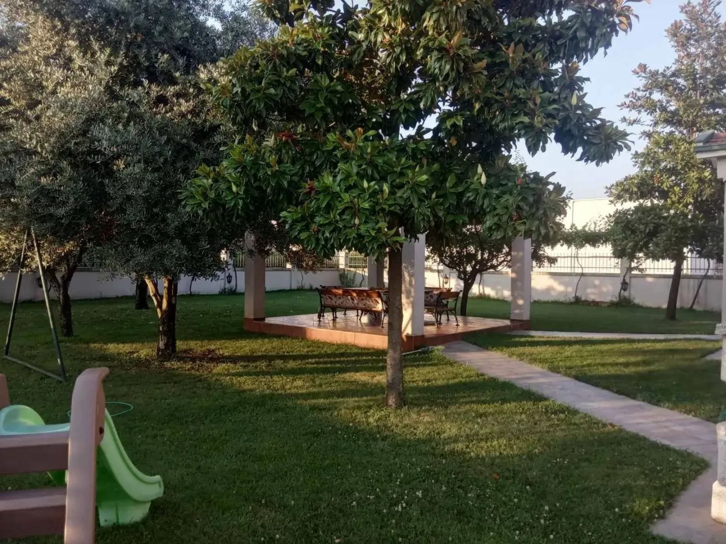 Landscaped yard with a lawn, trees, and a covered seating area.