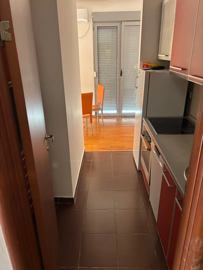 Pogled iz hodnika na kuhinju sa crvenimelementima i trpezariju sa izlazom na terasu.