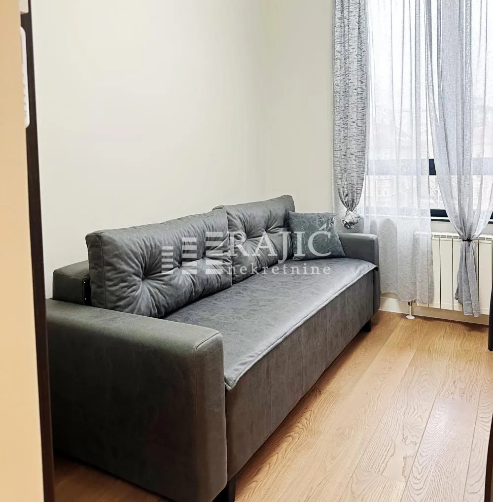 Living room with a grey sofa and a window with curtains.