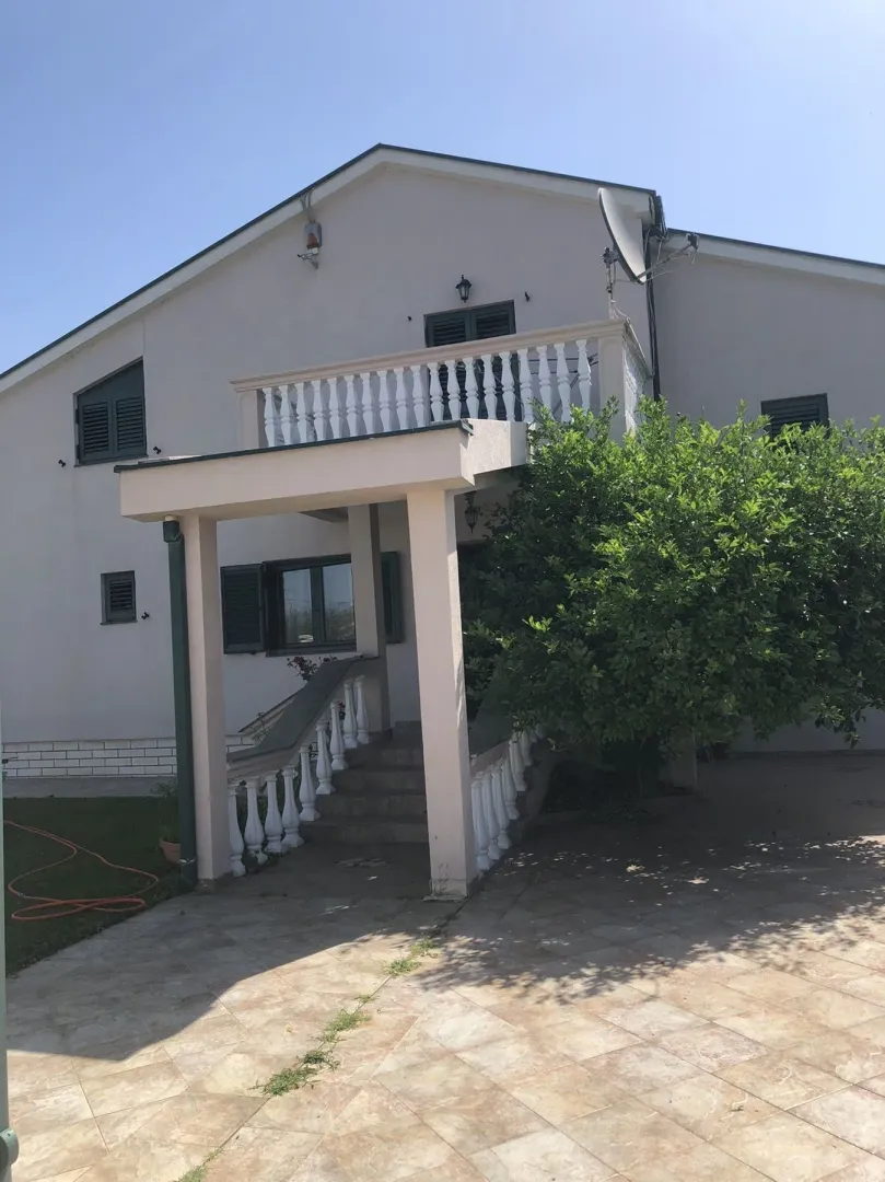 Exterior view of a two-story house with entrance stairs and a balcony.
