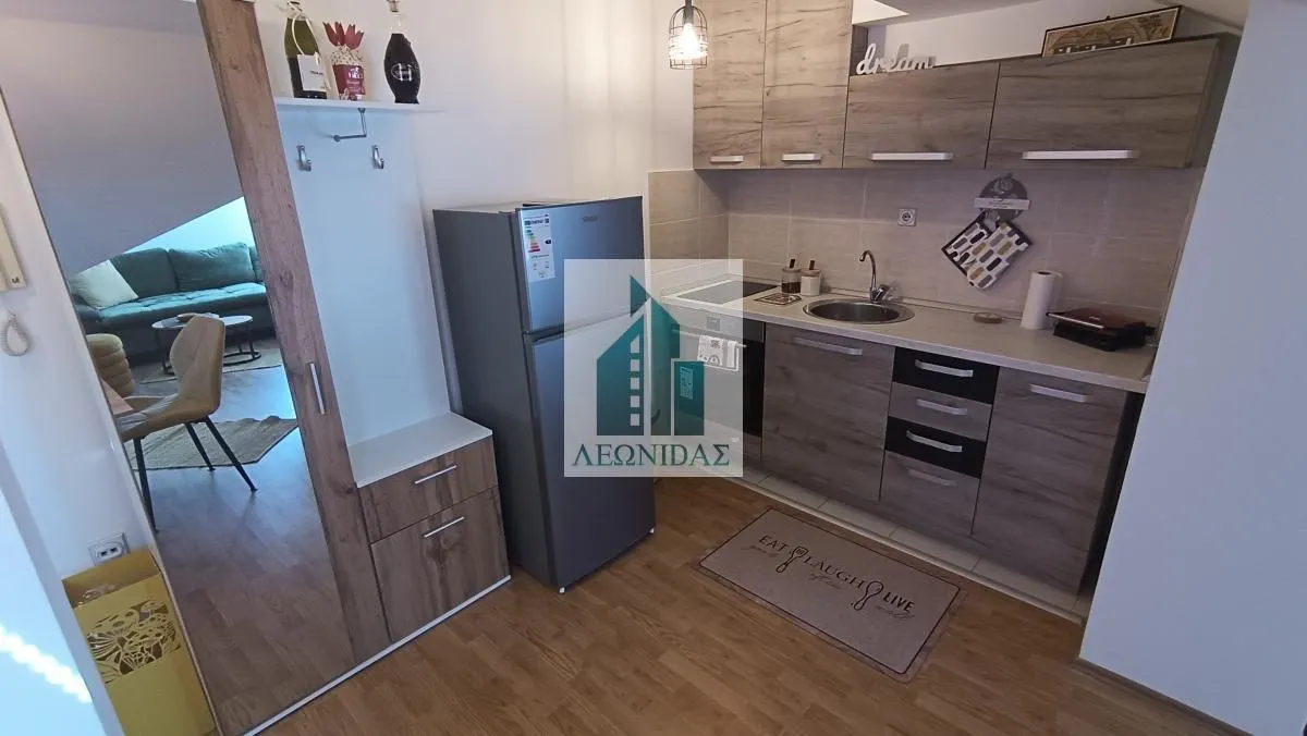 Compact kitchen with wooden cabinetry and refrigerator, connected to the living area.