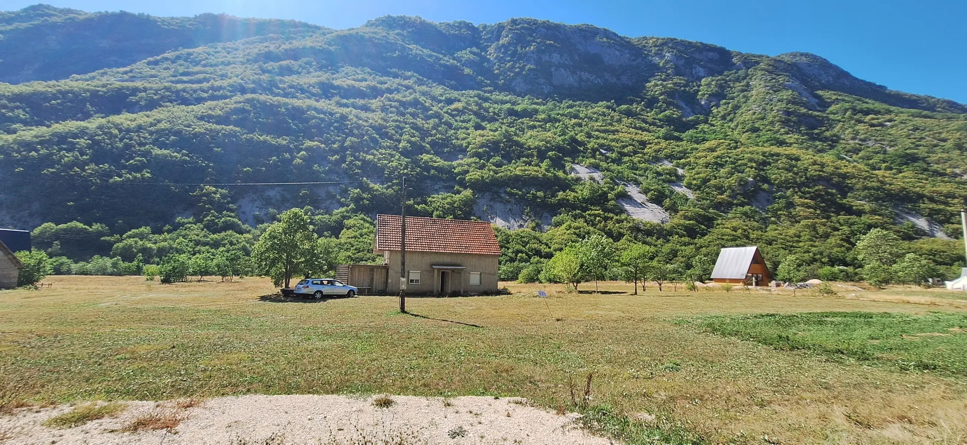 Pogled na kuću sa dvorištem i brdima u pozadini.