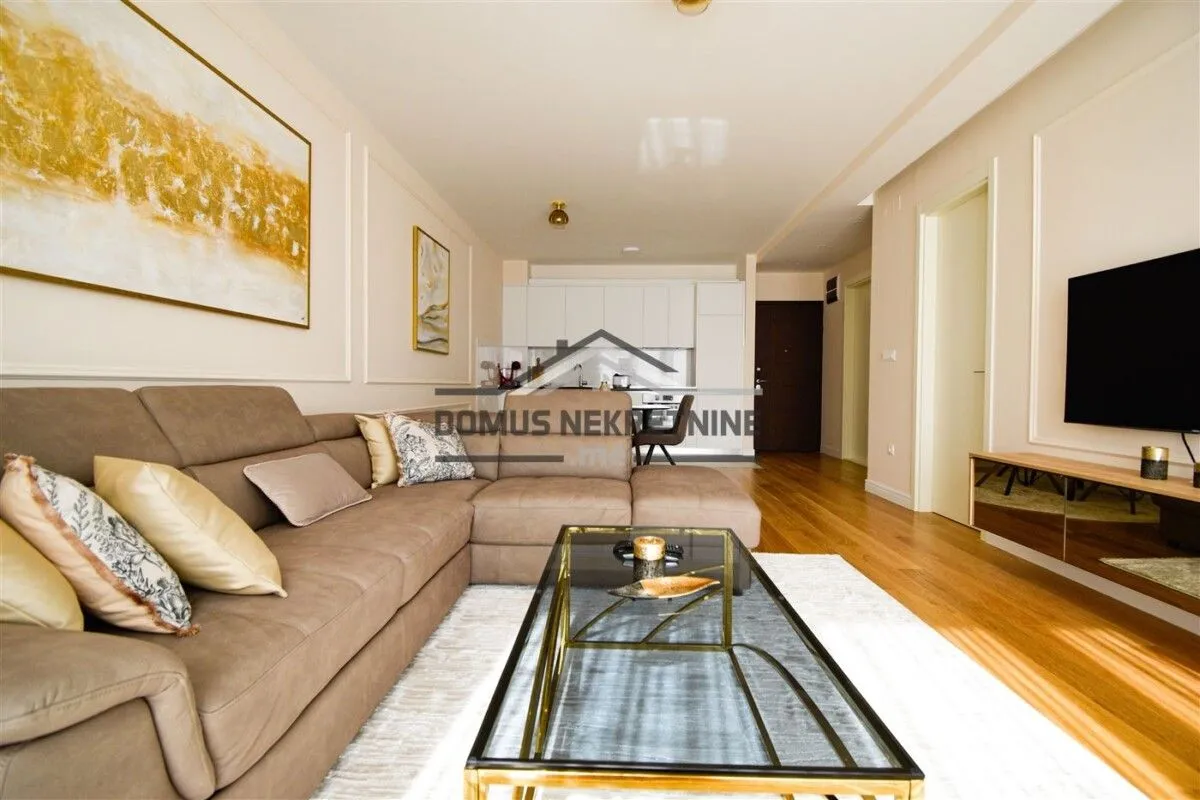Living room with a sectional sofa, coffee table and TV, with a view of the kitchen in the background.