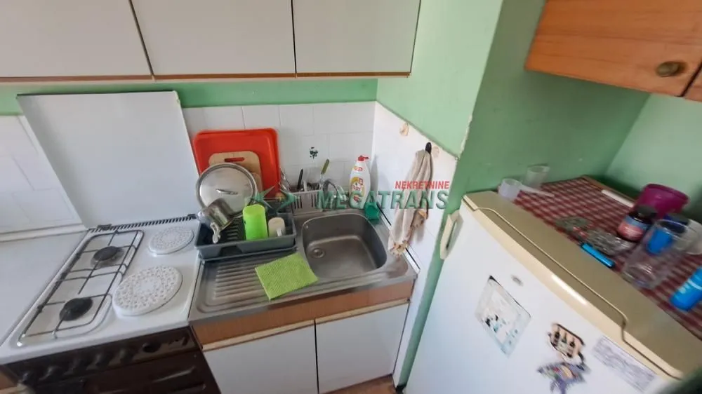 Pogled na deo kuhinje sa štednjakom, sudoperom i frižiderom.