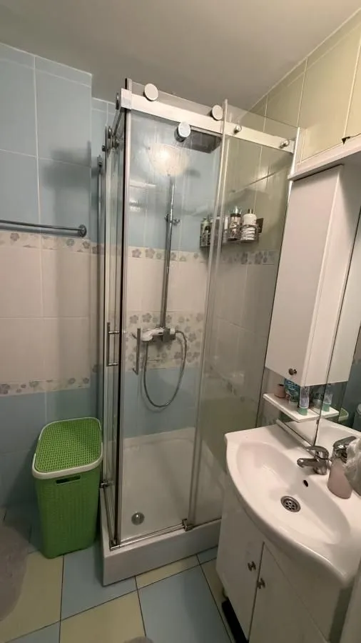 Kupatilo sa tuš kabinom, umivaonikom i pločicama na zidu.
