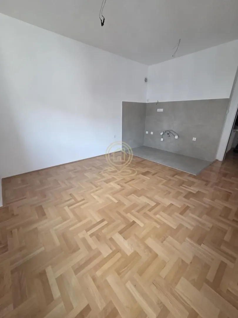 Nenamještena prostorija sa pripremljenim priključcima za kuhinju i parketom na podu.
