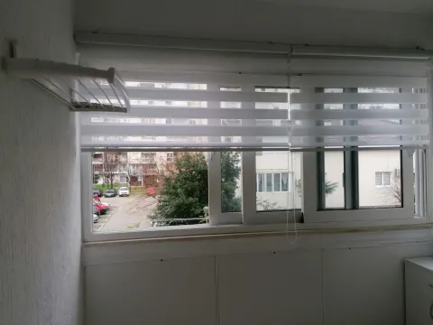 Pogled kroz prozor sa roletnama sa terase na okolne zgrade i parking. - image 9