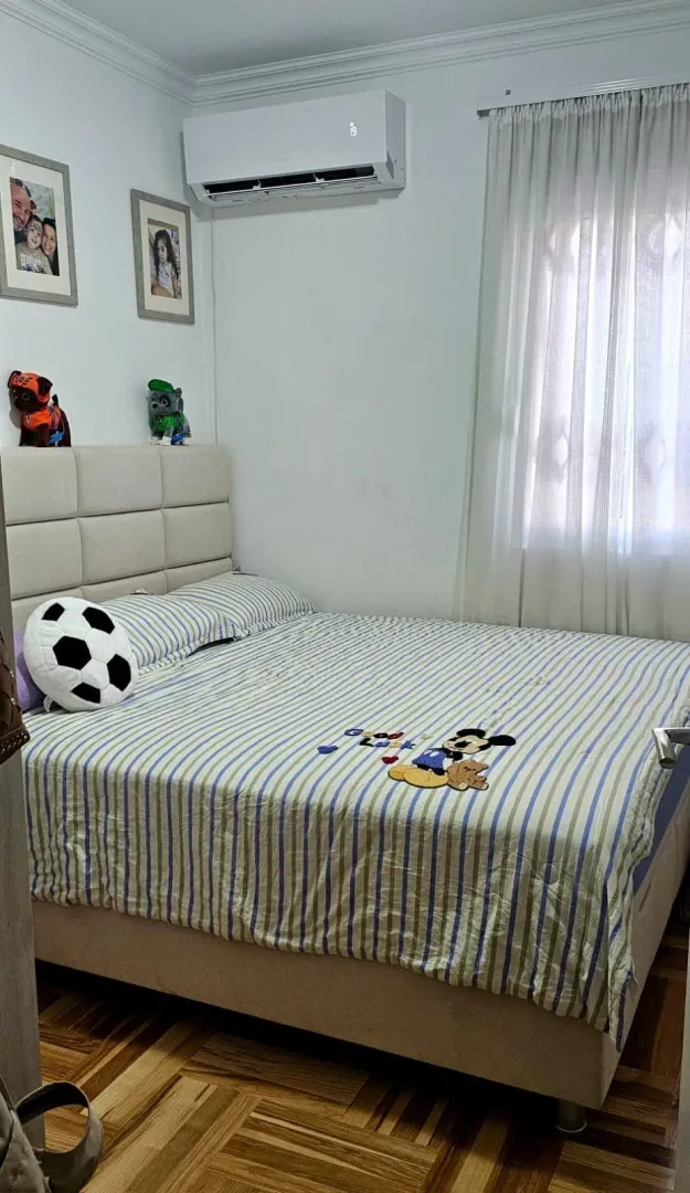 Spavaća soba sa bračnim krevetom, klima-uređajem i prozorom sa zavesama.
