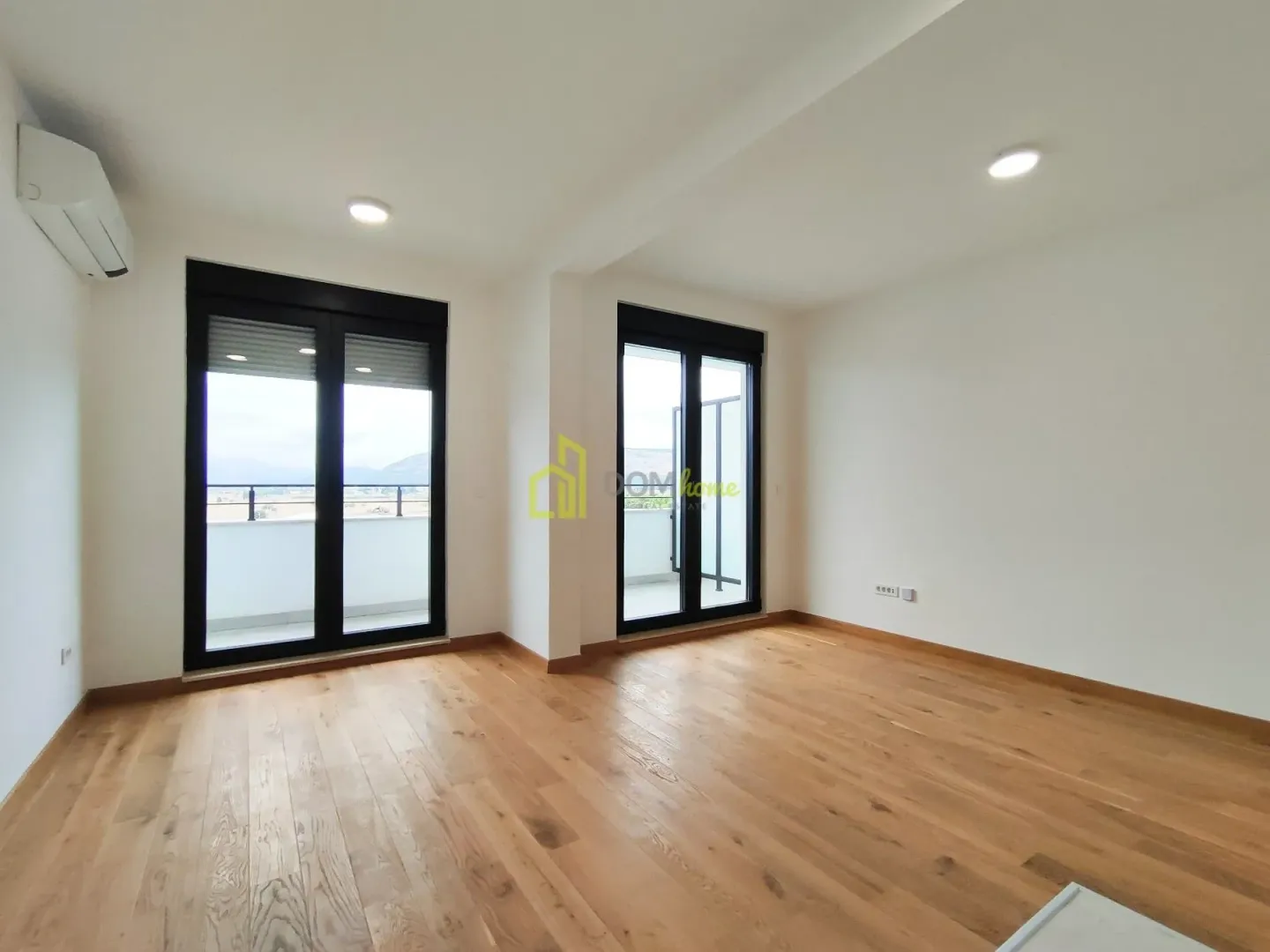Prazna soba sa drvenim podom i izlazom na balkon.