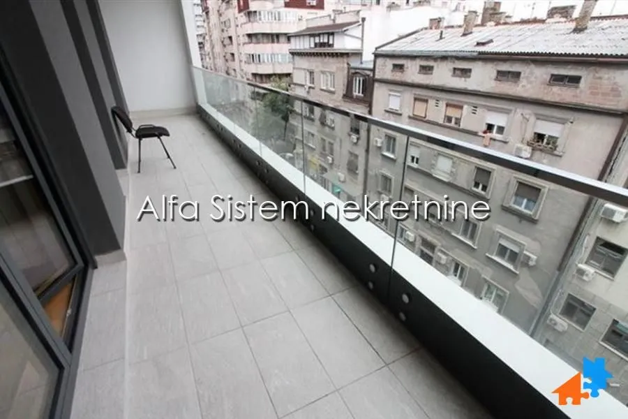 Dugačak popločani balkon sa staklenom ogradom i pogledom na grad.
