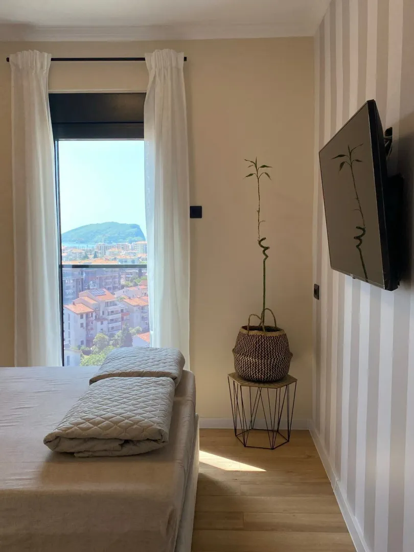 Bedroom with a bed, wall-mounted TV, and a view of the city through the window.
