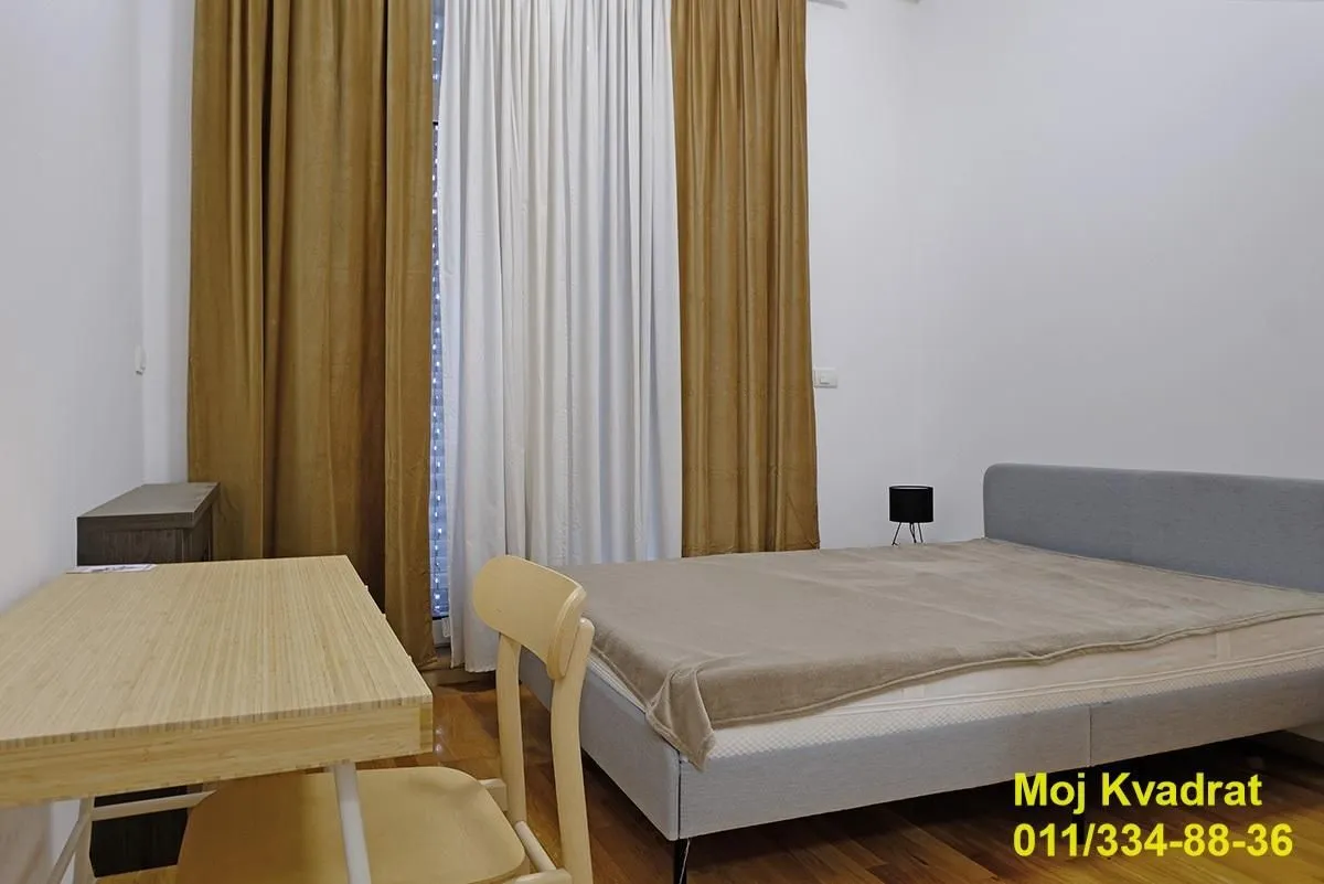 Spavaća soba sa bračnim krevetom, radnim stolom i prozorom sa zavesama.
