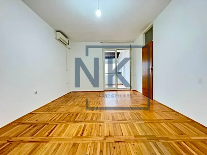 Prazna soba sa drvenim parketom i izlazom na terasu.