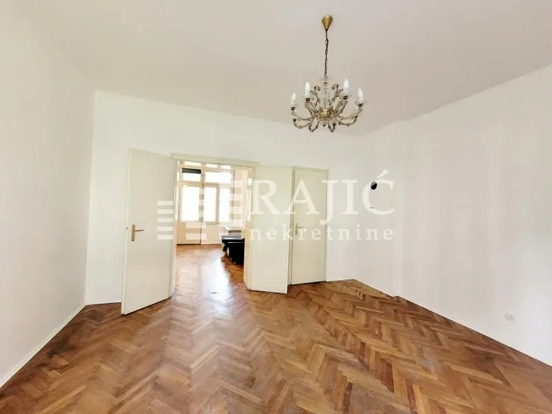 Empty room with parquet flooring and a chandelier in the apartment.