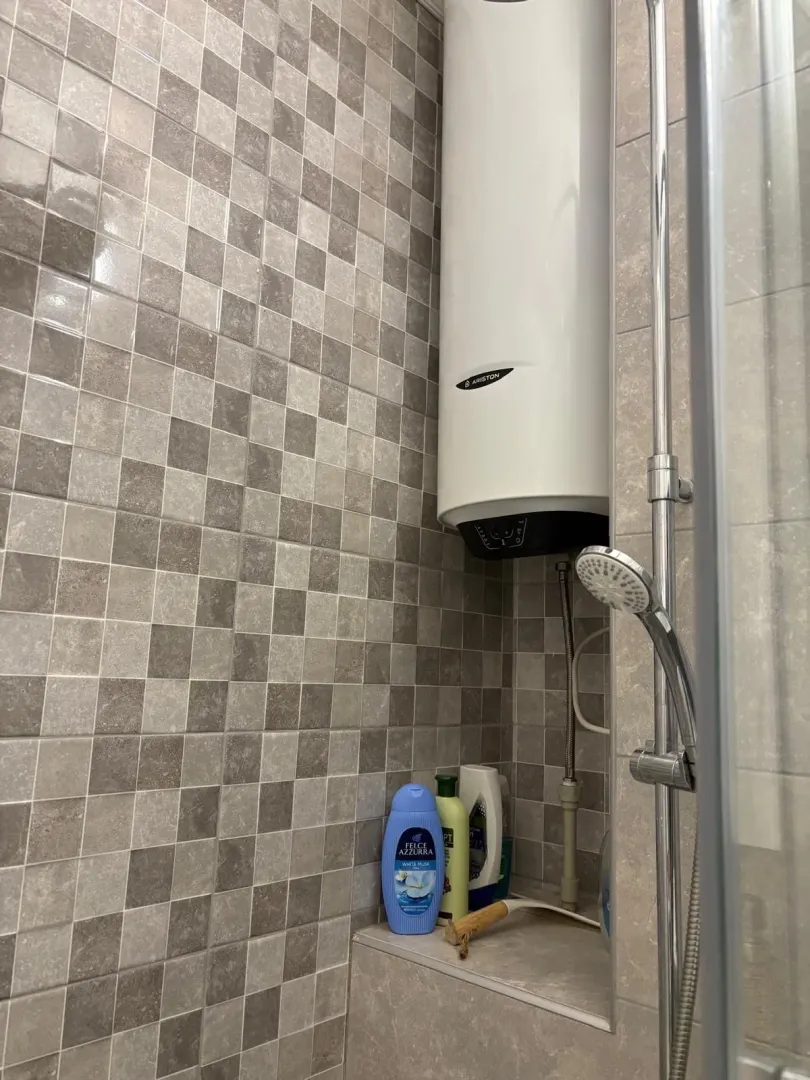 Part of a bathroom featuring a shower, water heater, and grey tiles.