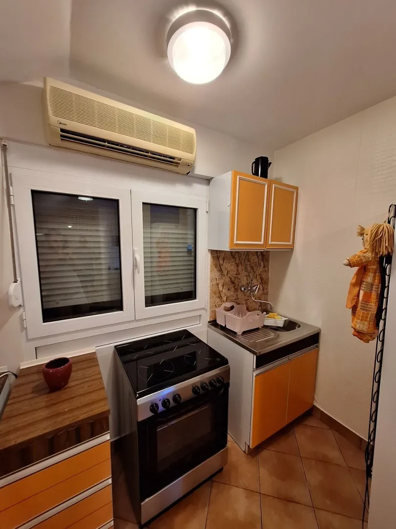 A small functional kitchen with orange cabinets, a stove, and an air conditioner.