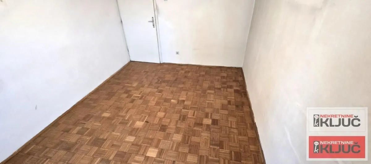 Prazna soba sa parketom na podu i belim zidovima.