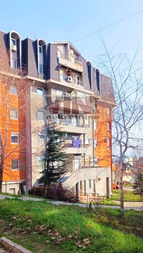 Pogled na spoljašnjost stambene zgrade sa balkonom i okruženjem.
