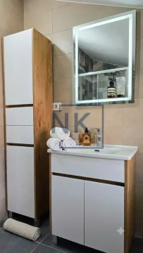 Bathroom with a vanity sink, lighted mirror, and wooden cabinet storage. - image 6