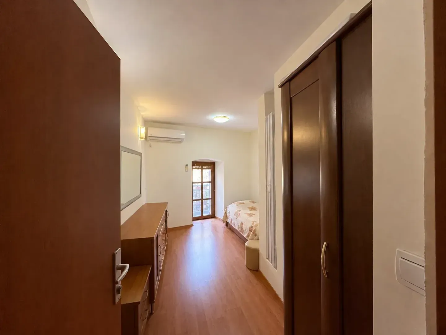 Pogled iz hodnika na spavaću sobu sa ormarom i krevetom.
