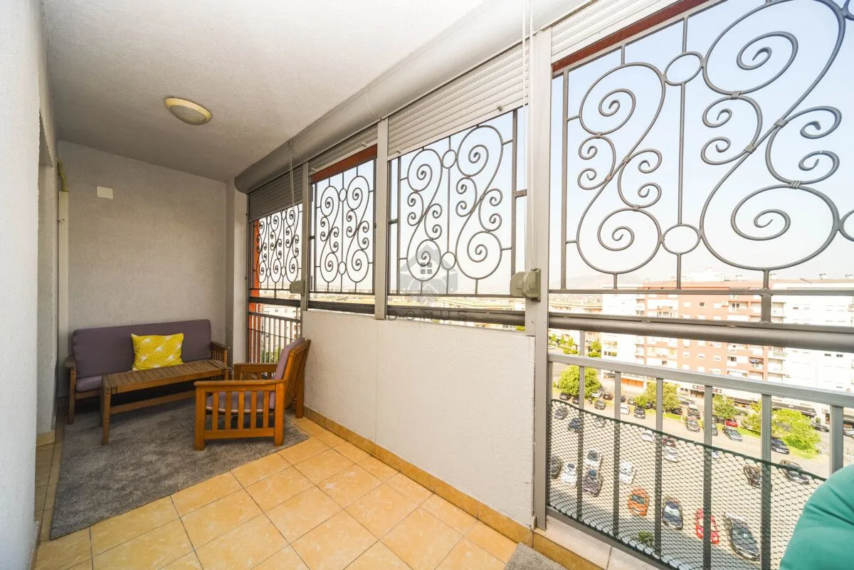 Enclosed balcony with seating furniture and a city view.