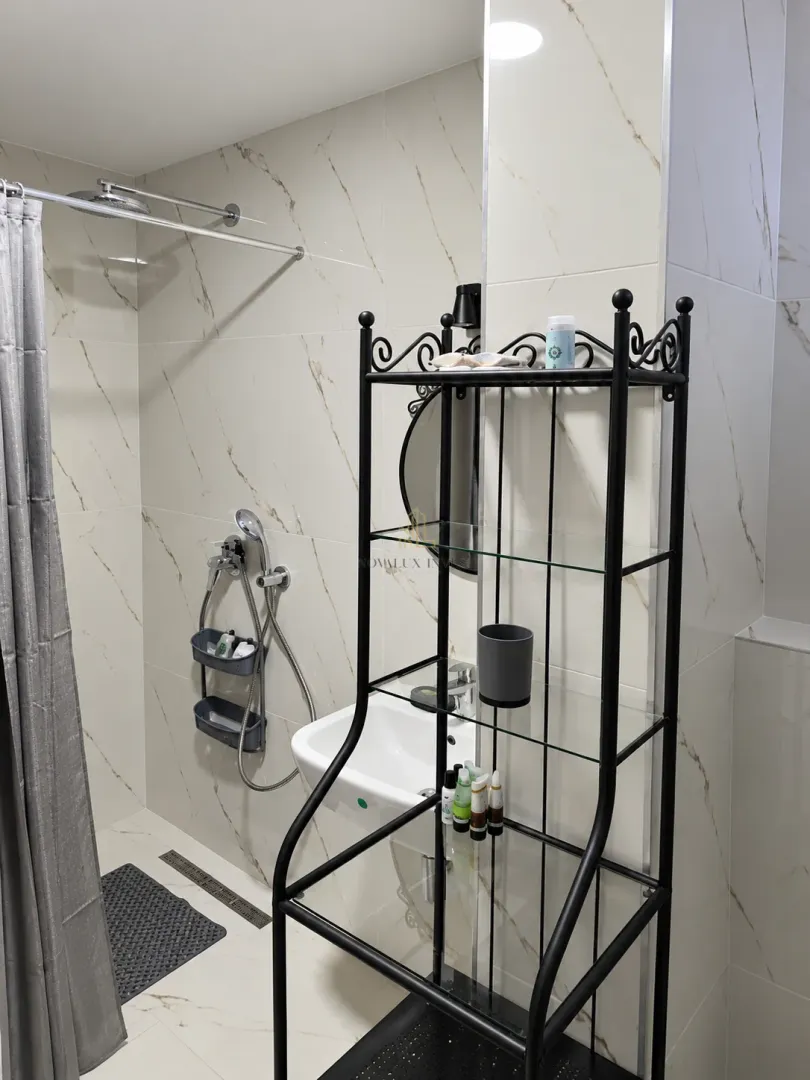 Small bathroom with a shower enclosure, washbasin, and a black metal shelving unit.