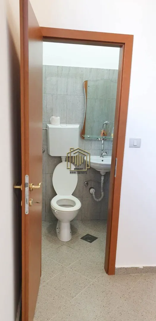 View through an open door into a small bathroom with a toilet, washbasin, and mirror.