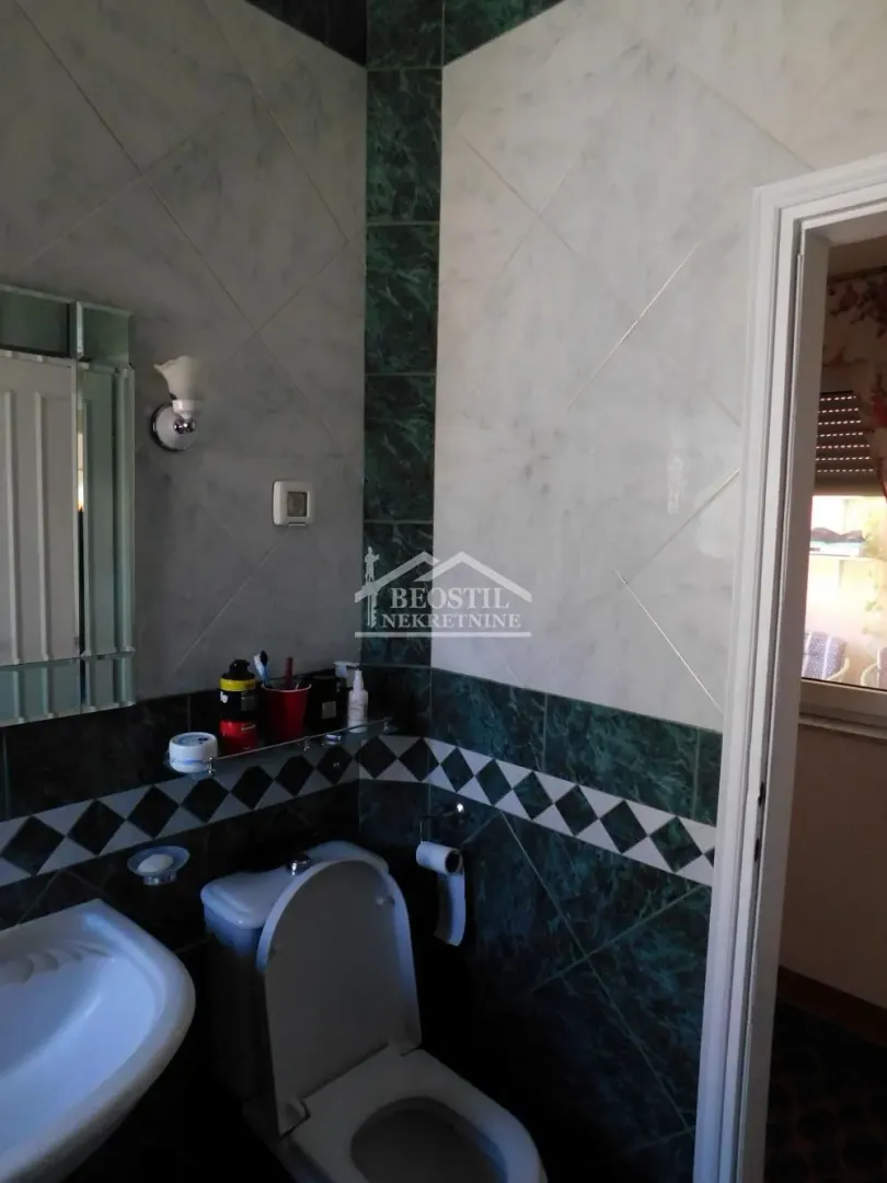 Manje kupatilo sa keramičkim pločicama, umivaonikom i wc šoljom.